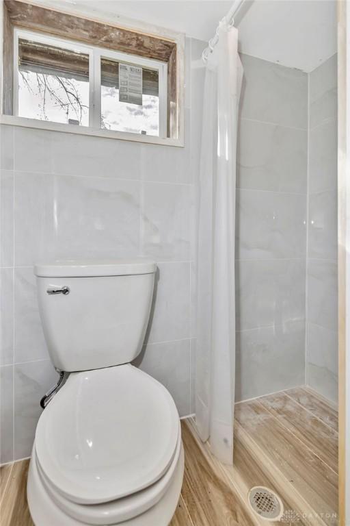 bathroom featuring a healthy amount of sunlight, curtained shower, wood-type flooring, and tile walls