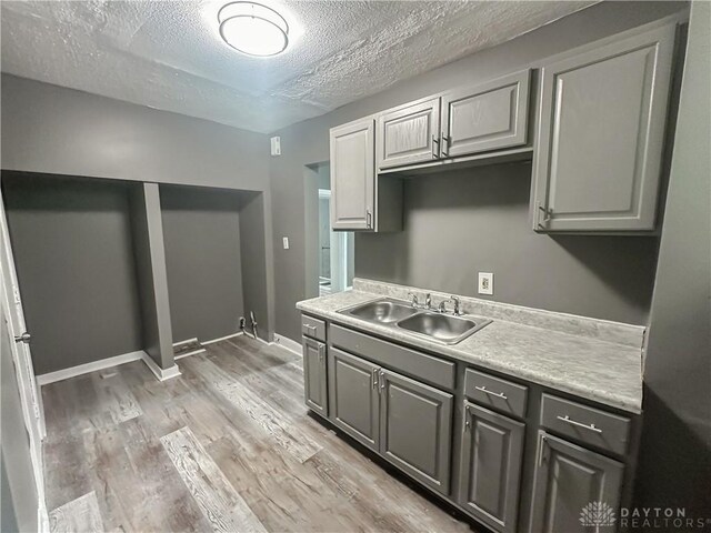 3501 Bevis Ave, Cincinnati, OH 45207 - kitchen with light wood finished floors, light countertops, gray cabinets, a sink, and a textured ceiling