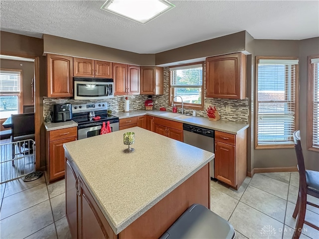 kitchen with appliances with stainless steel finishes, light tile patterned flooring, tasteful backsplash, a center island, and sink