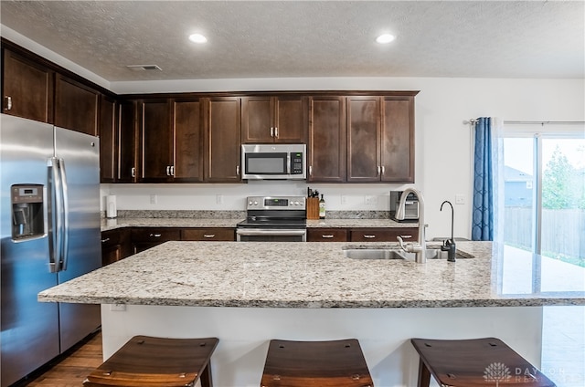 kitchen featuring light stone countertops, stainless steel appliances, a textured ceiling, and sink