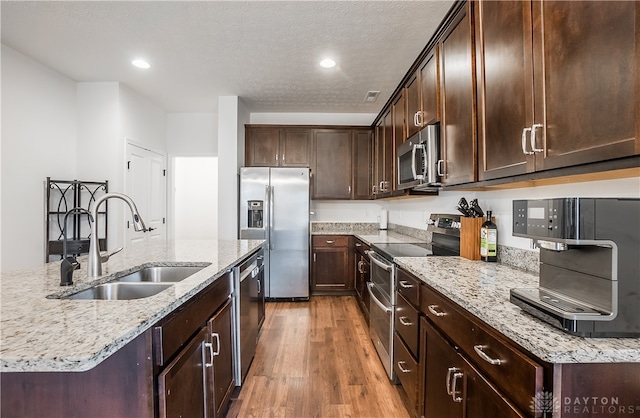 kitchen featuring sink, a textured ceiling, light hardwood / wood-style flooring, appliances with stainless steel finishes, and light stone countertops