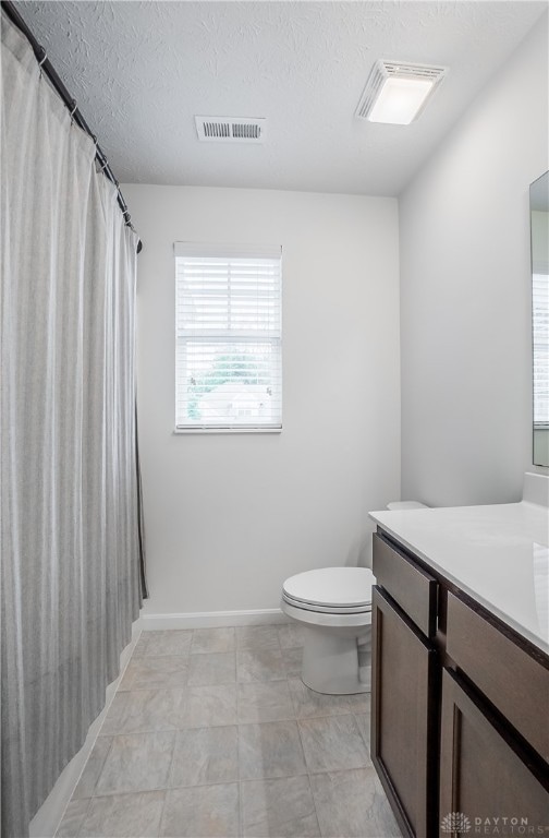 bathroom with a textured ceiling, vanity, toilet, and walk in shower