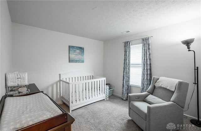 carpeted bedroom with a nursery area and a textured ceiling