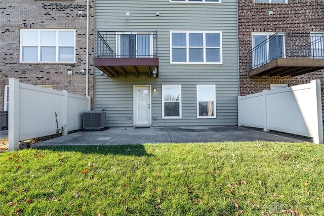 back of house with a balcony, central AC unit, a patio area, and a lawn