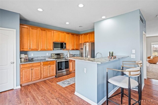 kitchen with a breakfast bar, light wood-type flooring, light stone counters, kitchen peninsula, and stainless steel appliances