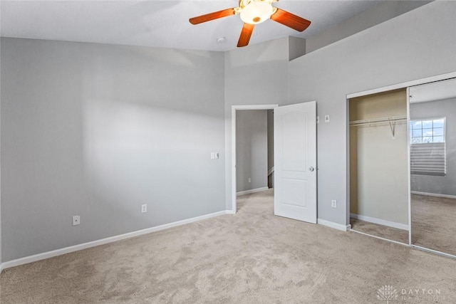 unfurnished bedroom with ceiling fan, a closet, a towering ceiling, and light colored carpet