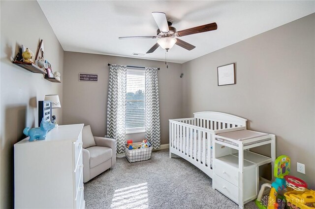 bedroom with ceiling fan, light colored carpet, and a crib