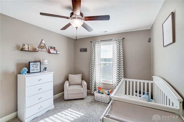 carpeted bedroom featuring ceiling fan and a crib