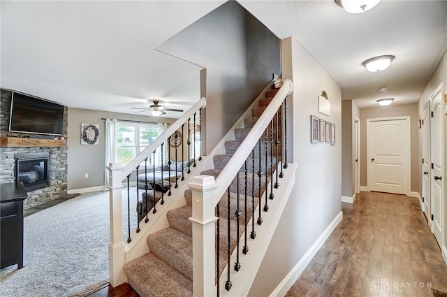 stairway with ceiling fan, a fireplace, and hardwood / wood-style flooring