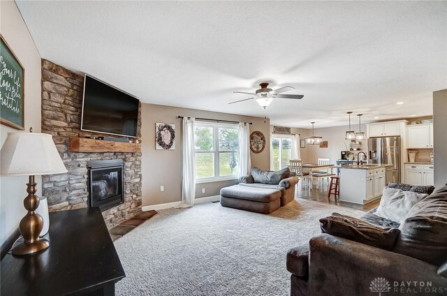 living room with a textured ceiling, light colored carpet, ceiling fan, sink, and a stone fireplace