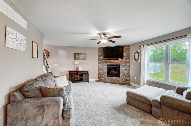 living room with carpet, a textured ceiling, a stone fireplace, and ceiling fan