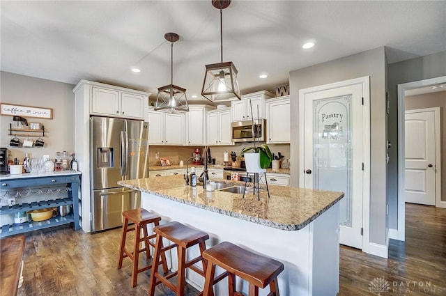 kitchen with a breakfast bar, stainless steel appliances, a kitchen island with sink, white cabinetry, and hanging light fixtures