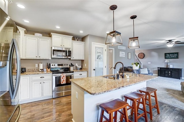 kitchen with a kitchen bar, stainless steel appliances, a kitchen island with sink, ceiling fan, and hanging light fixtures