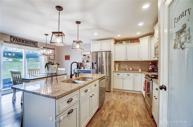 kitchen with stainless steel appliances, sink, pendant lighting, a center island with sink, and white cabinets