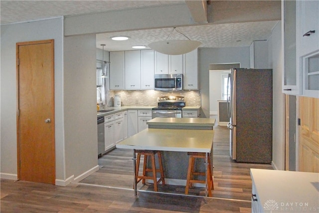 kitchen featuring white cabinets, stainless steel appliances, a breakfast bar area, and dark wood-type flooring