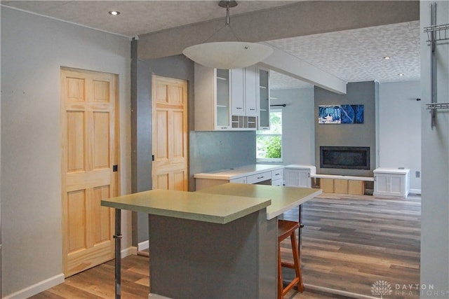 kitchen with white cabinets, kitchen peninsula, wood-type flooring, and a breakfast bar area