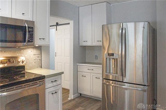 kitchen with white cabinets, appliances with stainless steel finishes, a barn door, and dark hardwood / wood-style flooring