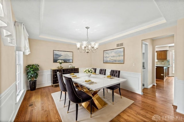 dining space featuring a tray ceiling, a chandelier, light hardwood / wood-style floors, and crown molding