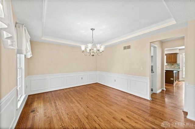 unfurnished room featuring a healthy amount of sunlight, a raised ceiling, wood-type flooring, and a chandelier