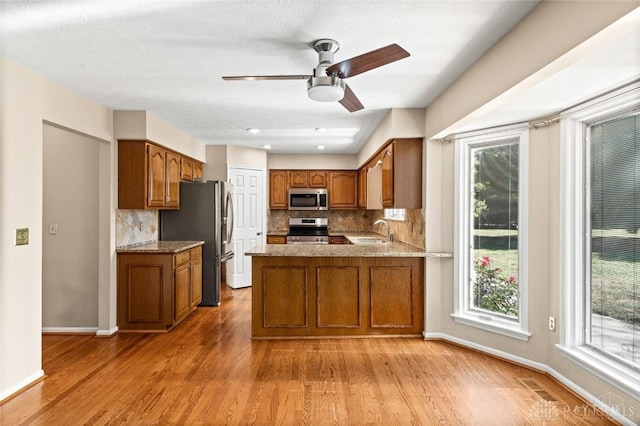 kitchen with kitchen peninsula, stainless steel appliances, ceiling fan, light hardwood / wood-style flooring, and sink