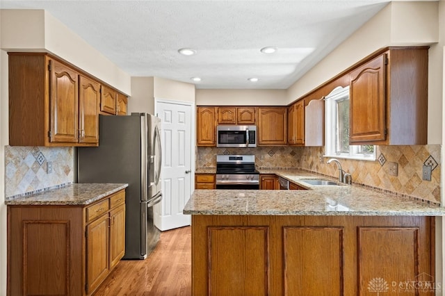 kitchen featuring light stone counters, sink, kitchen peninsula, stainless steel appliances, and light hardwood / wood-style floors