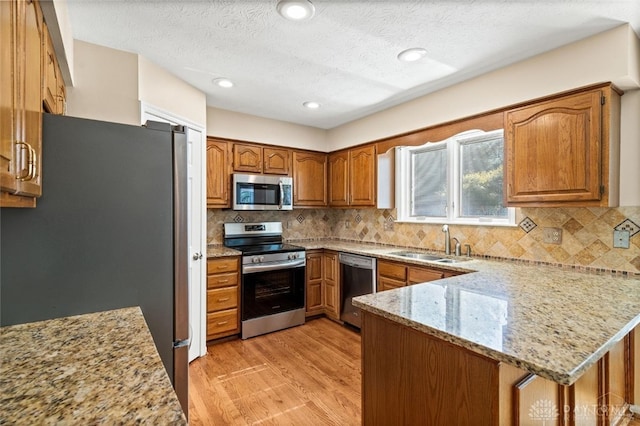 kitchen with sink, kitchen peninsula, light hardwood / wood-style flooring, backsplash, and stainless steel appliances