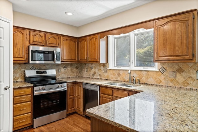 kitchen with light stone counters, sink, light hardwood / wood-style flooring, backsplash, and appliances with stainless steel finishes