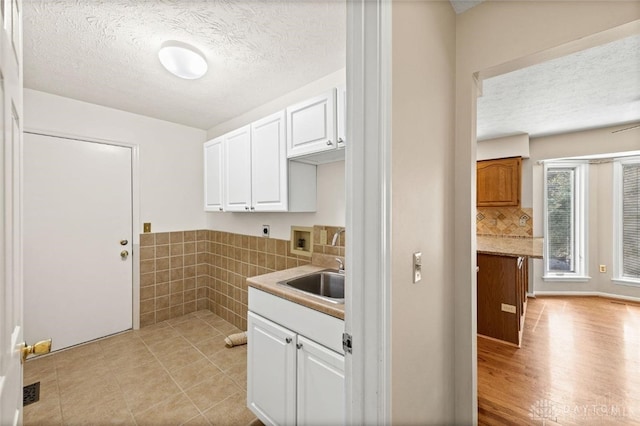 kitchen featuring white cabinets, a textured ceiling, light hardwood / wood-style flooring, and sink