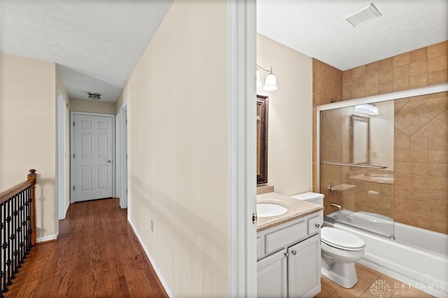 full bathroom with vanity, a textured ceiling, shower / bath combination with glass door, hardwood / wood-style flooring, and toilet