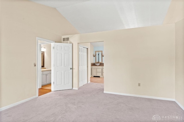 unfurnished bedroom featuring light carpet, vaulted ceiling, a closet, and ensuite bathroom