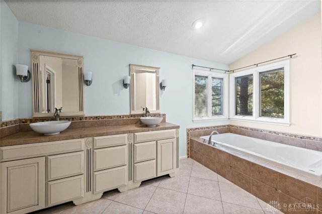 bathroom with tile patterned flooring, a textured ceiling, vaulted ceiling, a relaxing tiled tub, and vanity