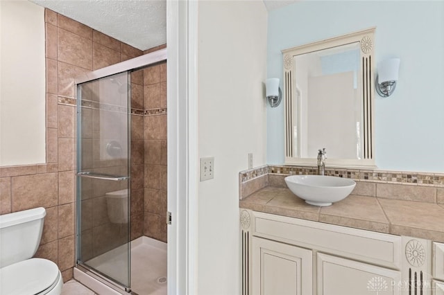 bathroom featuring tile walls, vanity, a textured ceiling, a shower with door, and toilet