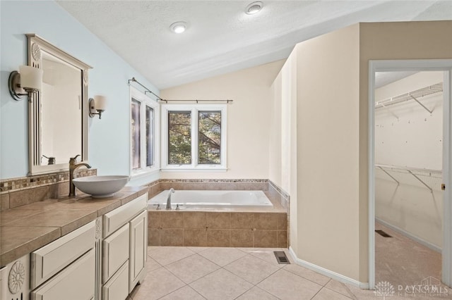 bathroom featuring tile patterned flooring, a textured ceiling, vaulted ceiling, a relaxing tiled tub, and vanity