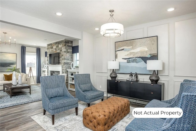 living area with an inviting chandelier, a stone fireplace, and hardwood / wood-style floors