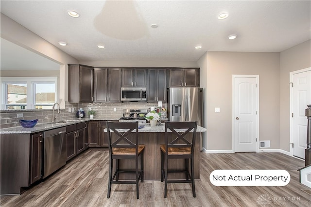 kitchen featuring dark wood-type flooring, sink, light stone counters, a center island, and appliances with stainless steel finishes