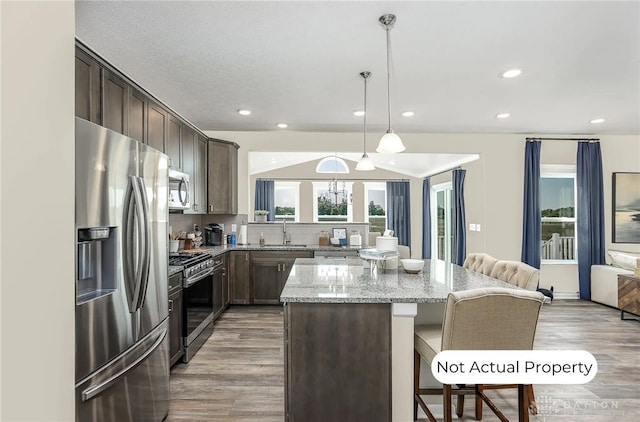 kitchen with pendant lighting, sink, stainless steel appliances, light stone countertops, and a kitchen island