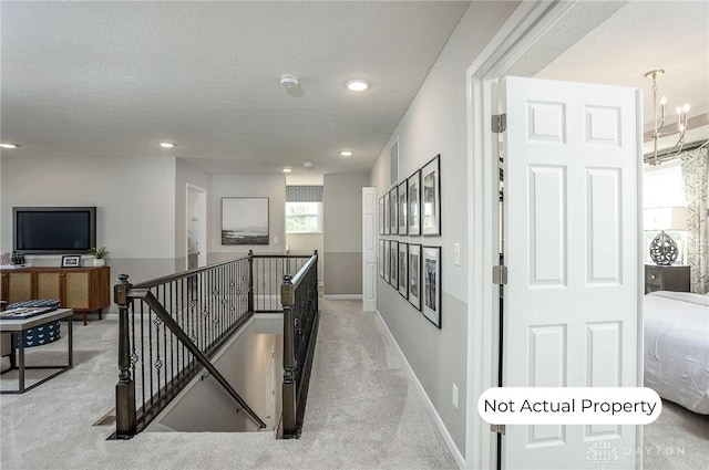 hallway with an inviting chandelier, light colored carpet, and a textured ceiling