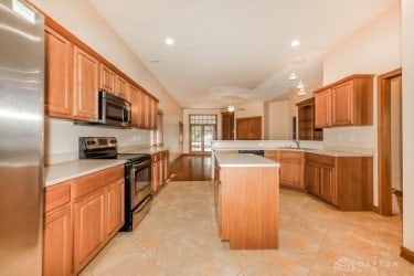 kitchen with sink, kitchen peninsula, a kitchen island, appliances with stainless steel finishes, and light tile patterned floors