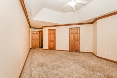 unfurnished bedroom featuring a tray ceiling, ceiling fan, carpet flooring, and crown molding