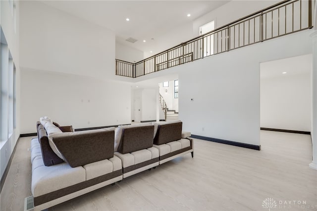 living room with a healthy amount of sunlight, light hardwood / wood-style floors, and a towering ceiling