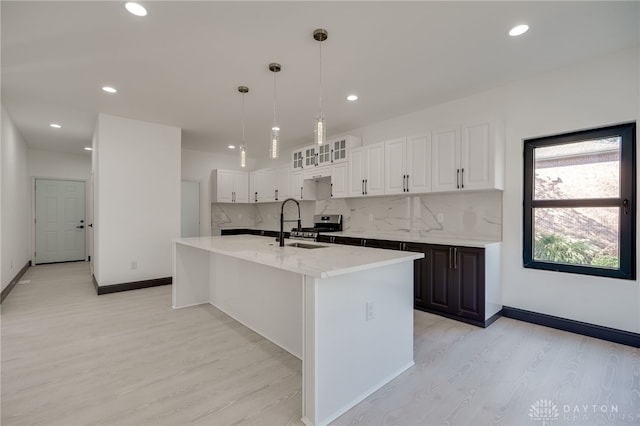 kitchen with backsplash, an island with sink, light hardwood / wood-style flooring, white cabinets, and pendant lighting