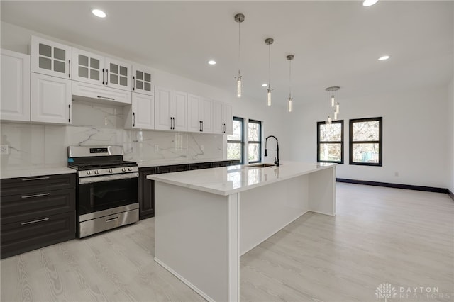 kitchen featuring tasteful backsplash, an island with sink, stainless steel stove, light stone countertops, and white cabinetry