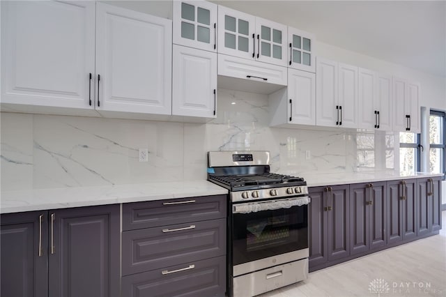 kitchen featuring stainless steel range with gas stovetop, tasteful backsplash, light stone countertops, white cabinetry, and light wood-type flooring