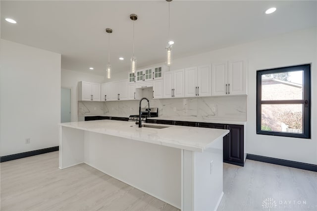 kitchen featuring tasteful backsplash, light stone counters, a center island with sink, white cabinetry, and light hardwood / wood-style floors