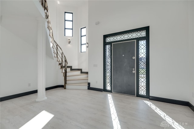 foyer entrance featuring a high ceiling, ornate columns, and light hardwood / wood-style flooring