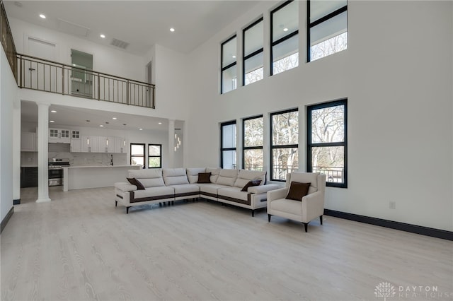 living room featuring a high ceiling, light wood-type flooring, and decorative columns