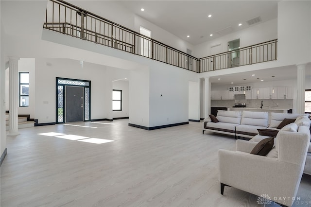 living room with ornate columns, a wealth of natural light, a high ceiling, and light hardwood / wood-style flooring