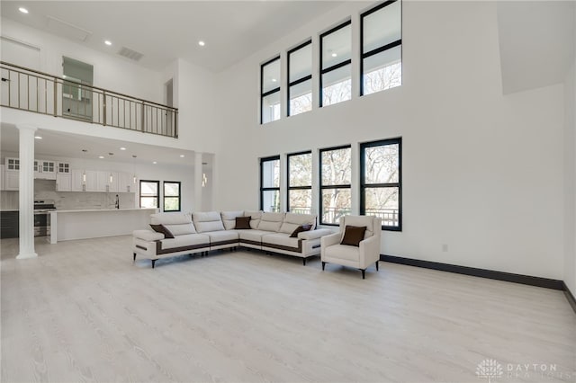 living room with light hardwood / wood-style floors, a high ceiling, and decorative columns