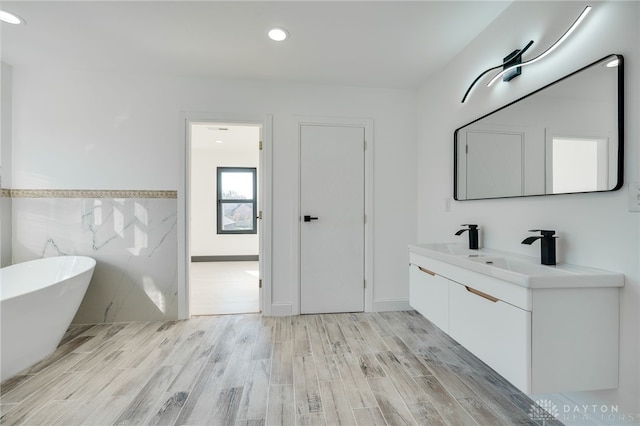 bathroom with a tub to relax in, vanity, and wood-type flooring