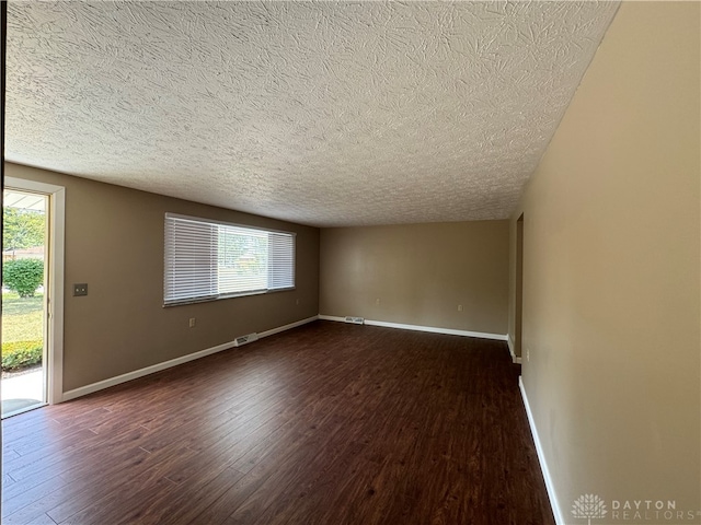 spare room with a textured ceiling and dark hardwood / wood-style floors